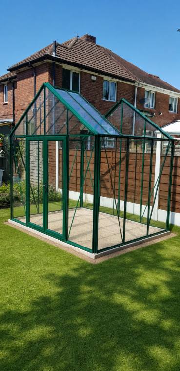 Green aluminium greenhouse newly erected on a fresh paved base in a Manchester garden